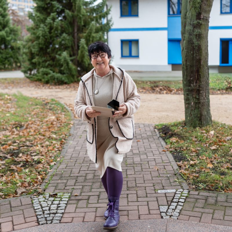 Mitarbeiterin einer Steuerkanzlei geht im Freien auf dem Kanzleigelände und hält Tablet und Smartphone in der Hand