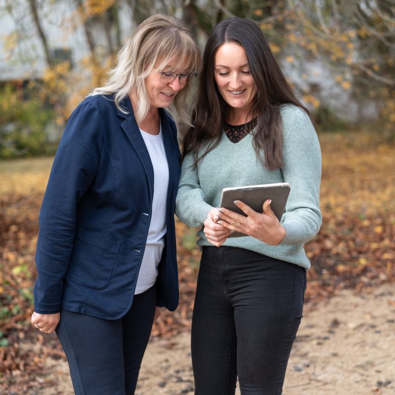 Zwei Mitarbeiterinnen einer Steuerkanzlei stehen im Freien und betrachten gemeinsam Inhalte auf einem Tablet